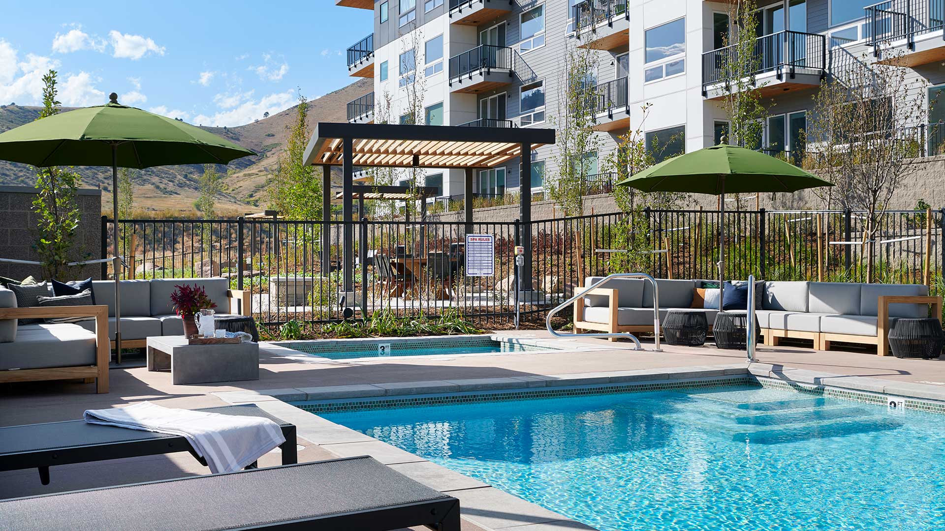 Epoque Golden outdoor spa and pool area with lounge seating, umbrellas, apartment balconies and foothill views.