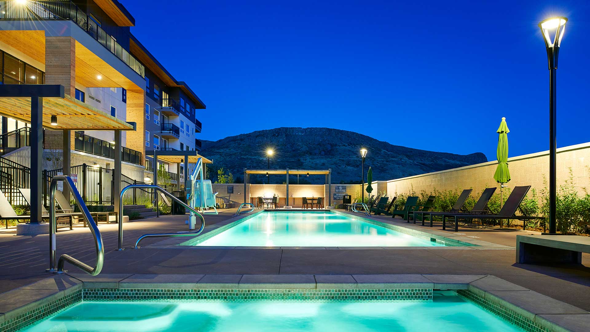 Epoque Golden outdoor pool and spa at dusk with lounge chairs, illuminated water and foothill views.