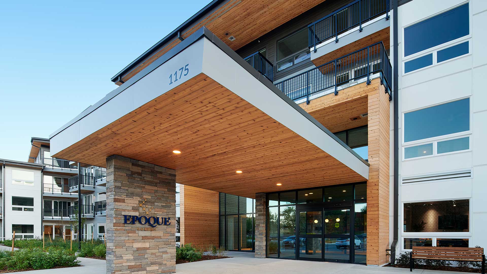 Main entrance of Epoque Golden apartments with covered porte-cochere, wood ceiling, stone columns and glass entry doors.