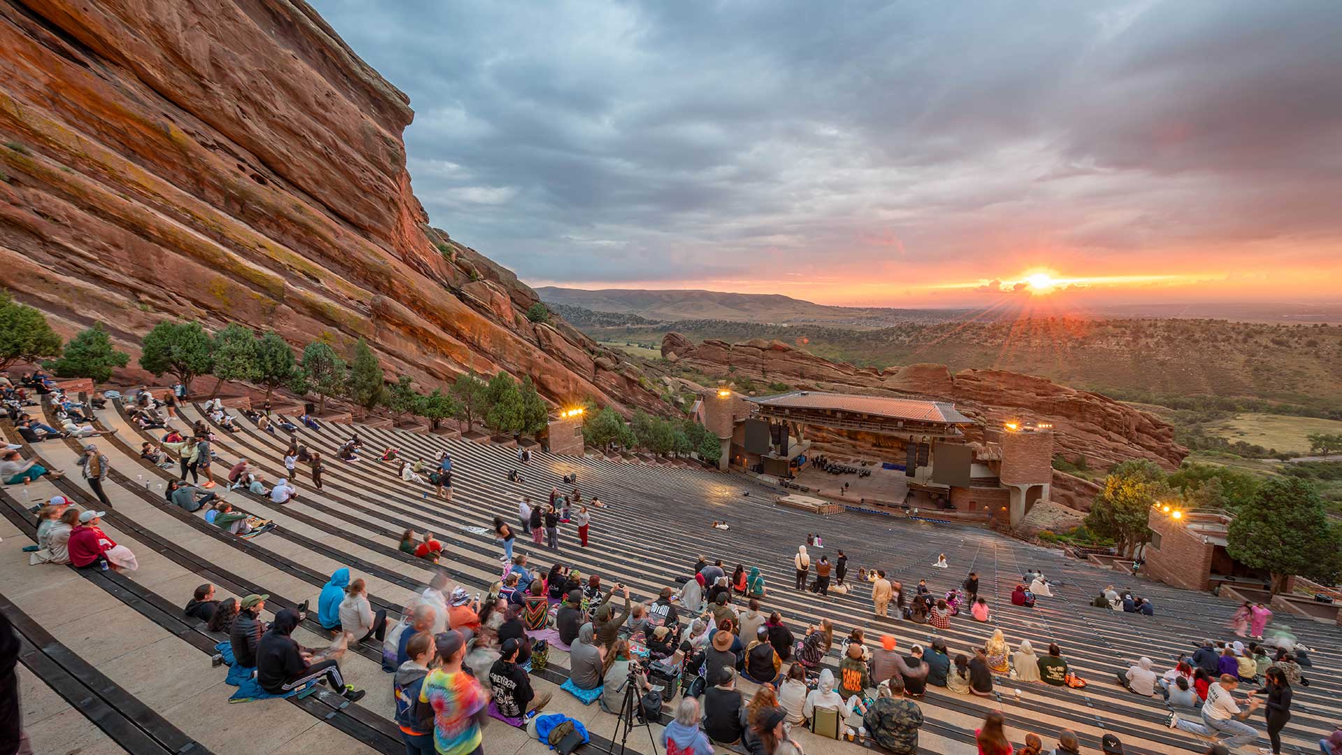 Red Rocks Amphitheatre at sunset with concertgoers seated among dramatic red rock formations west of Denver.
