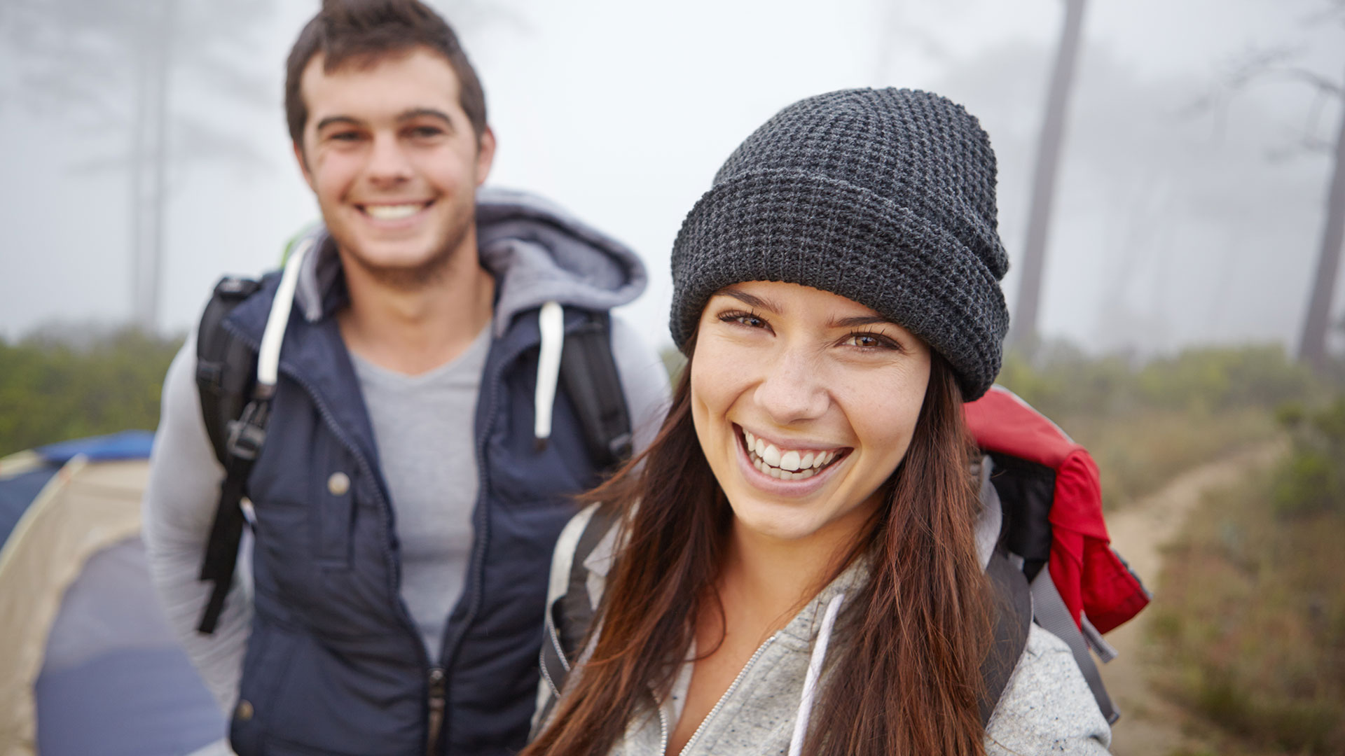 Smiling couple with backpacks enjoying a hiking and camping trip outdoors.